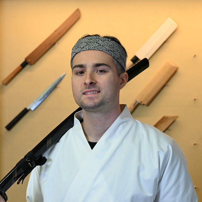 Ethan, founder of Smart Sushi Chef, in front of the knife wall